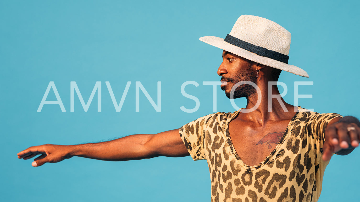 Side view of a young man wearing a straw hat dancing in studio against a blue background