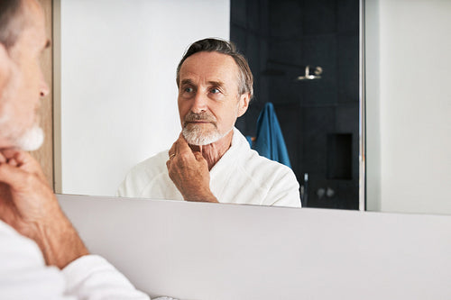 Handsome male in bathrobe inspecting his skin at morning