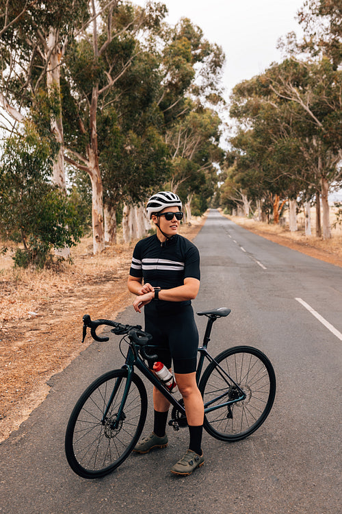 Cyclist checking smartwatch while taking a break on empty country road