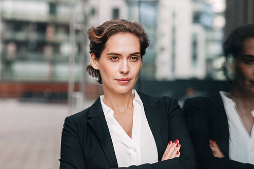 Confident businesswoman looking away. Portrait of young female in formal wear posing outdoors at office building with arms crossed.