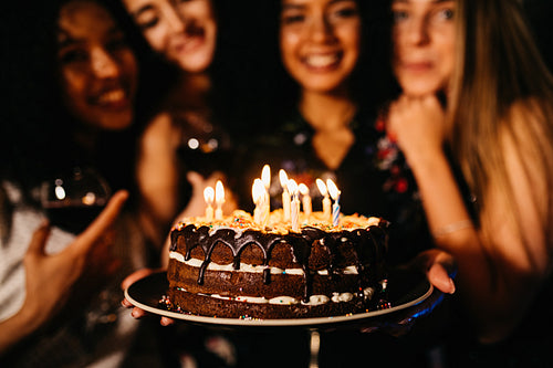 Close up shot of woman holding birthday cake standing indoors with friends