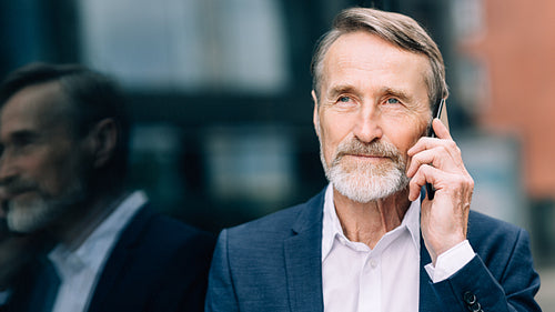 Serious bearded businessman talking on a mobile phone while standing outdoors