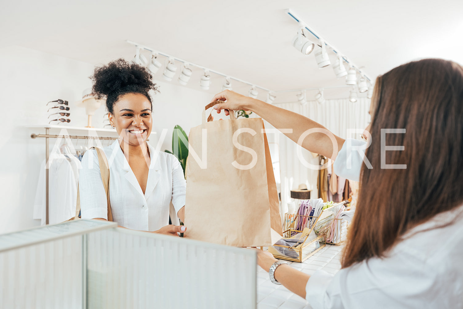 Smiling female customer receiving shopping bag from clothing store cashier