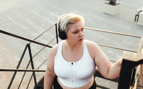 Young woman in headphones stepping up on staircase outdoors and looking away