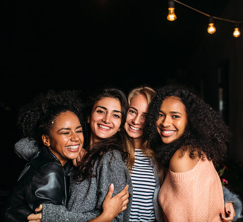 Group of four laughing female friends embracing at night