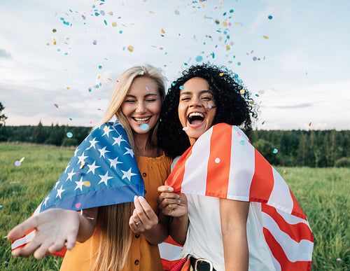 Two happy women standing outdoors under confetti with USA flag