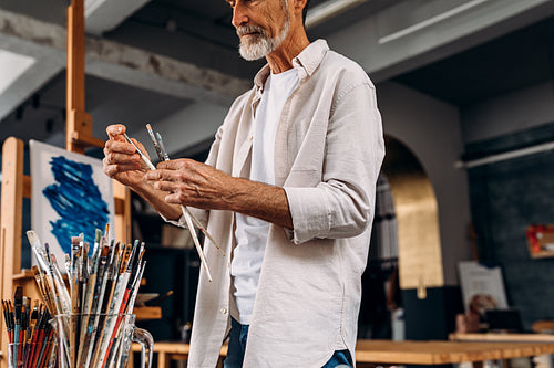 Male painter standing in his studio and observing quality of paint brushes before drawing