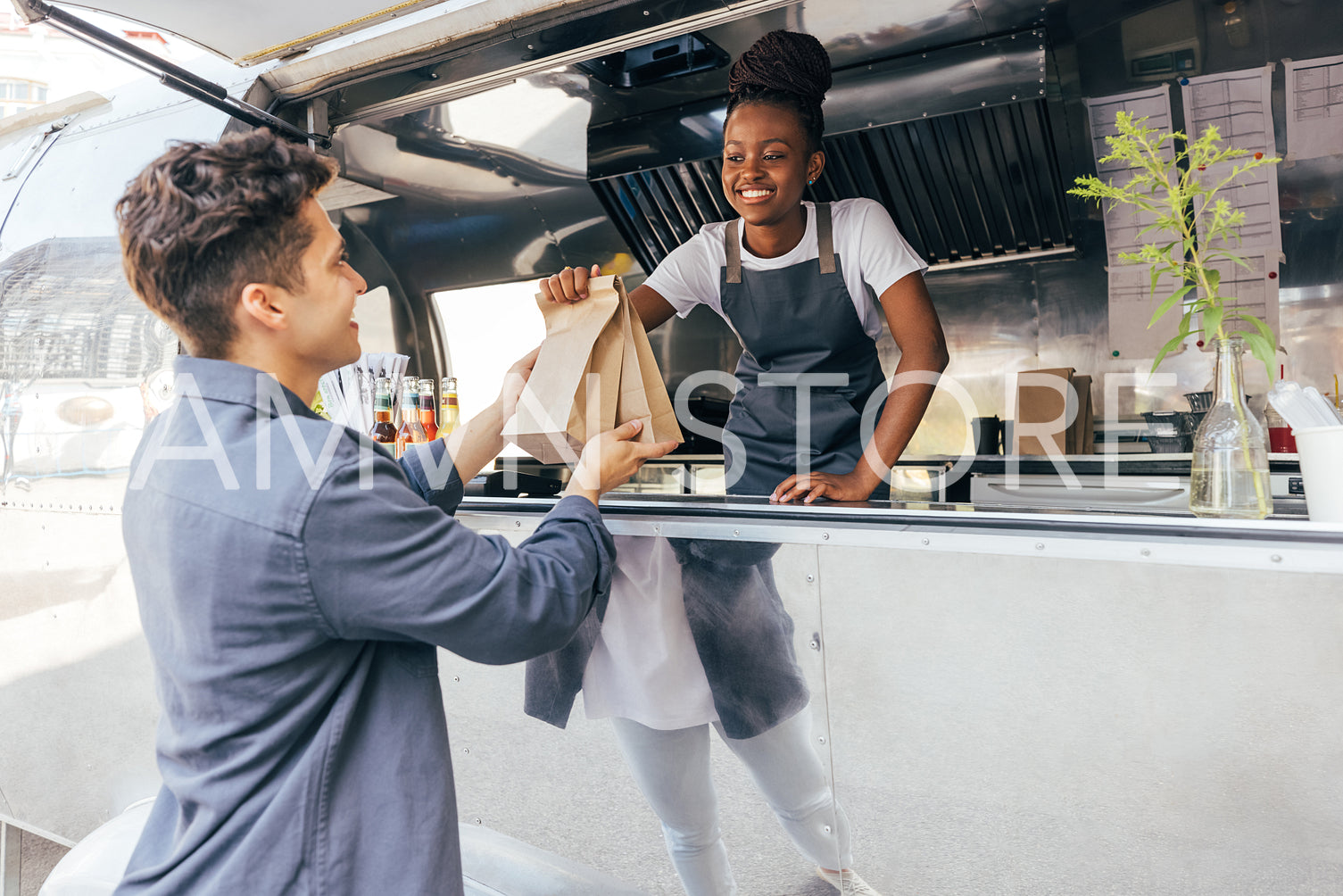 Side view of a young man taking packages with street food from a saleswoman