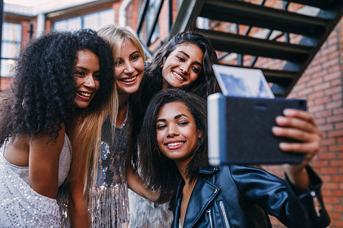 Four happy female friends taking an instant photo. Group of women taking selfie on instant camera outdoors.