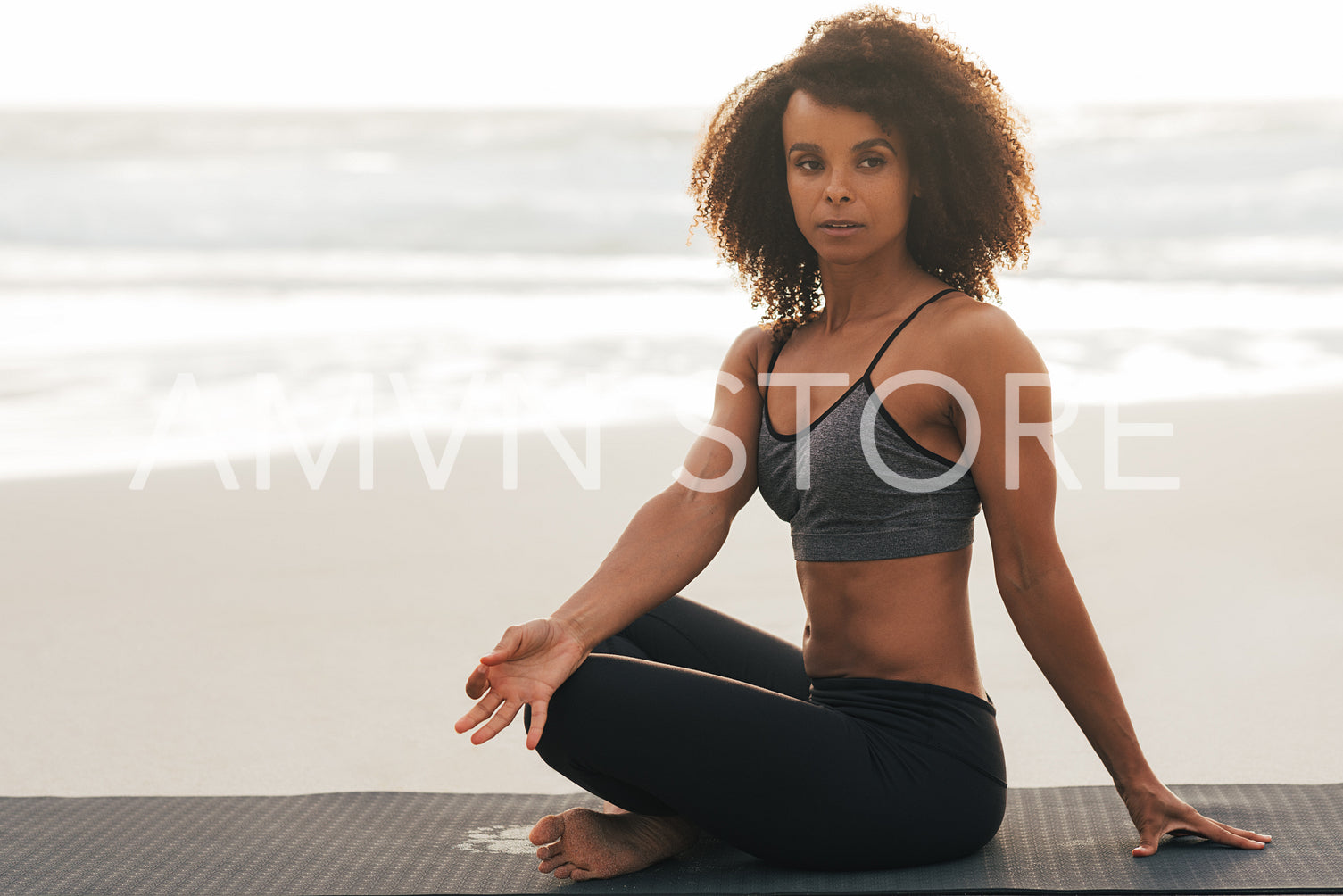 Young woman with crossed legs doing meditation practice at sunset. Healthy female sitting on mat doing yoga exercises.