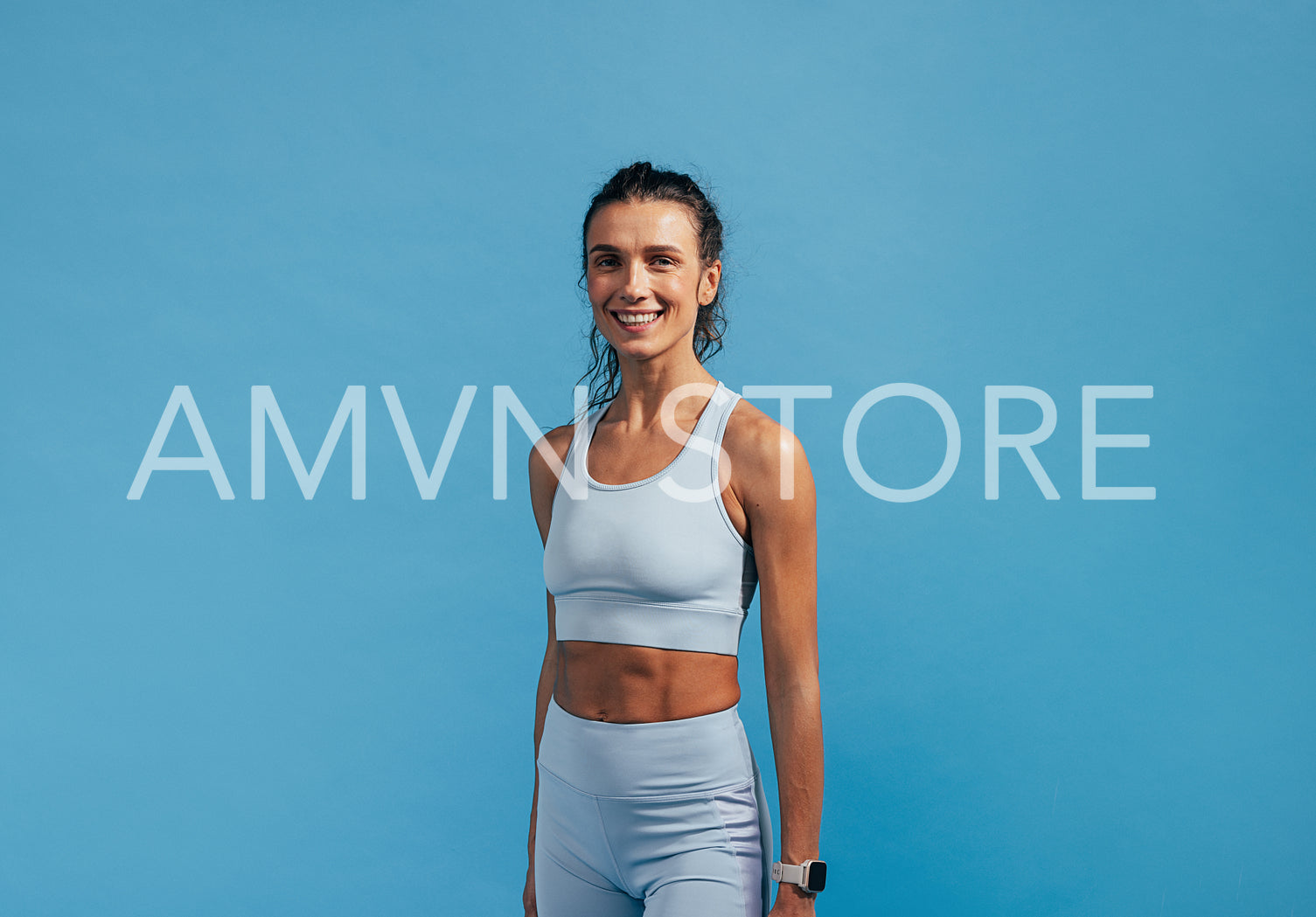 Portrait of young fitness female in sportswear looking at camera while standing on blue background