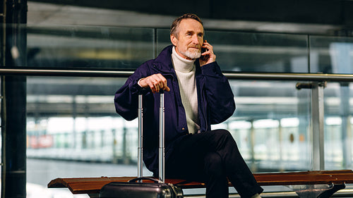 Senior tourist sitting at airport terminal and talking on cell phone