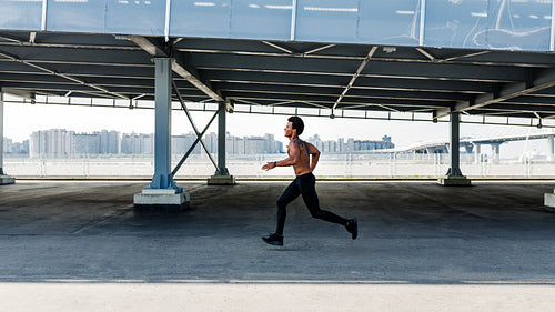 Side view of athletic bare chested man jogging outdoors on sidewalk