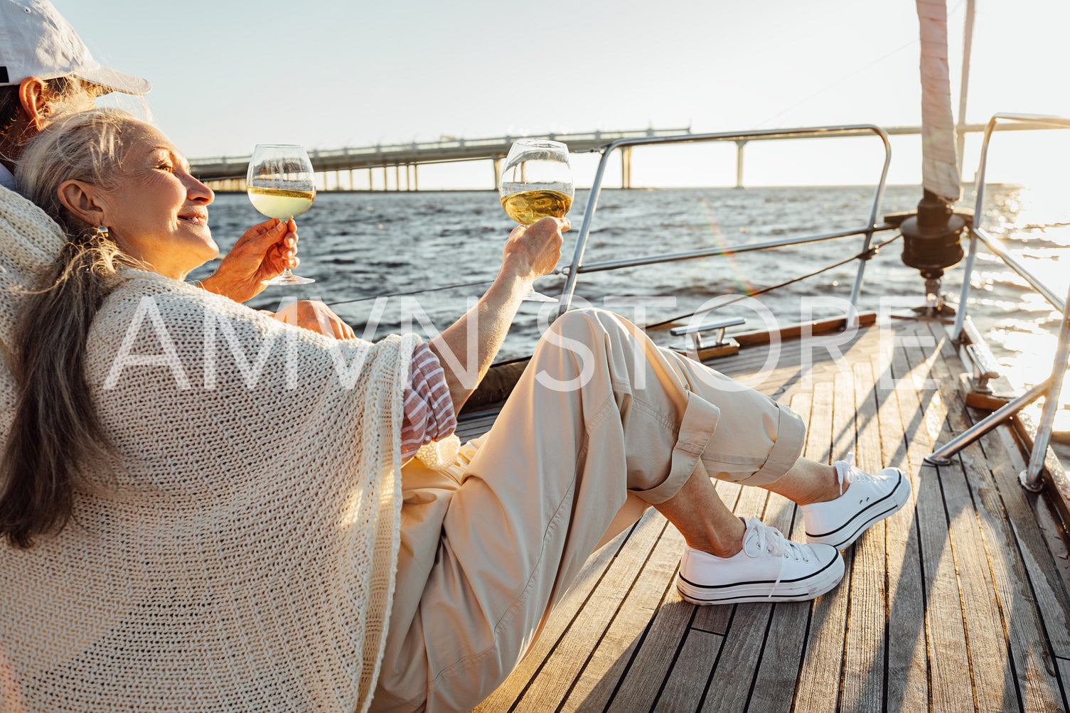 Mature man and woman wrapped in plaid on yacht deck and drinking wine. Senior couple holding glasses of wine on sailbot.	