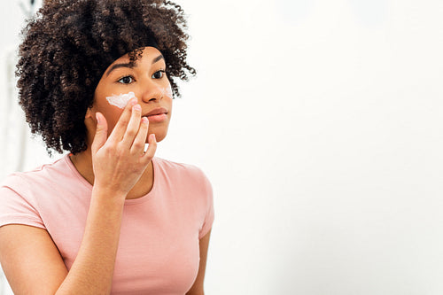 Young woman applying moisturizer cream on her face