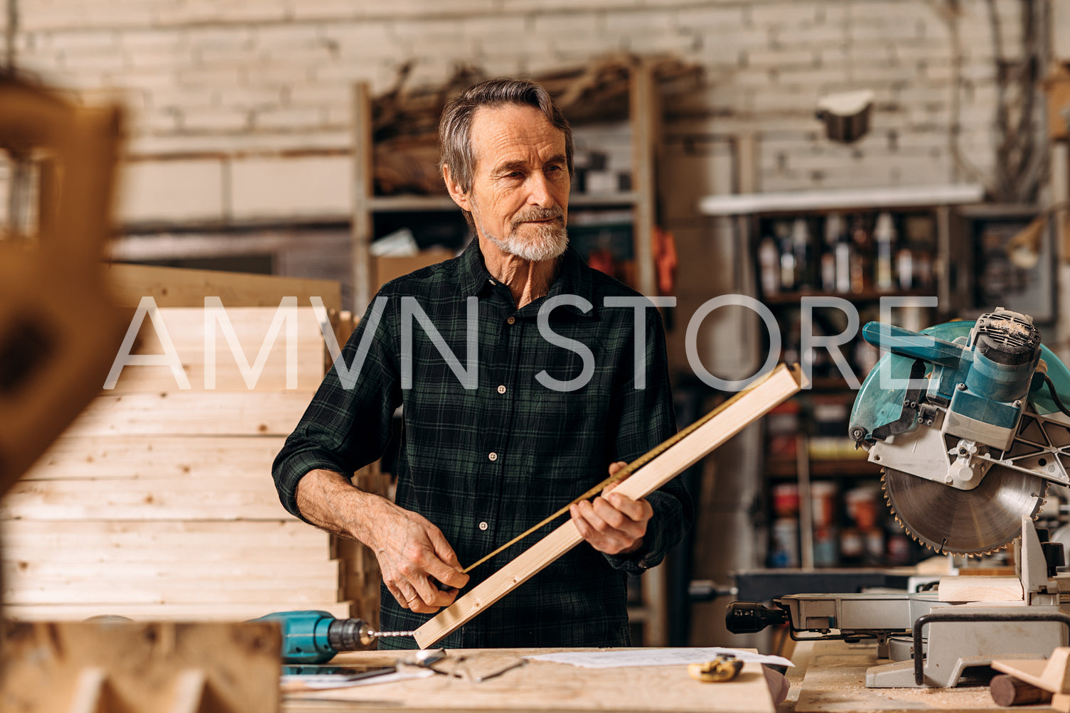 Mature carpenter measuring a length of wooden plank in workshop	