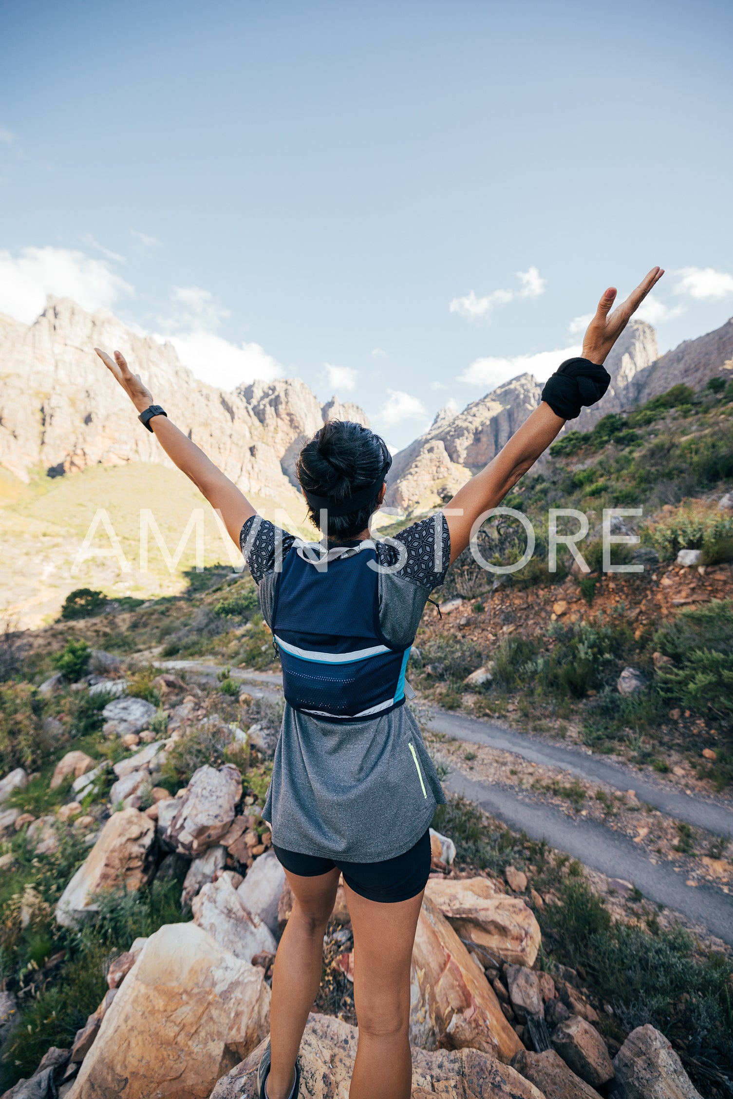 Rear view of young female standing in valley with raised arms. Young woman enjoying hike.