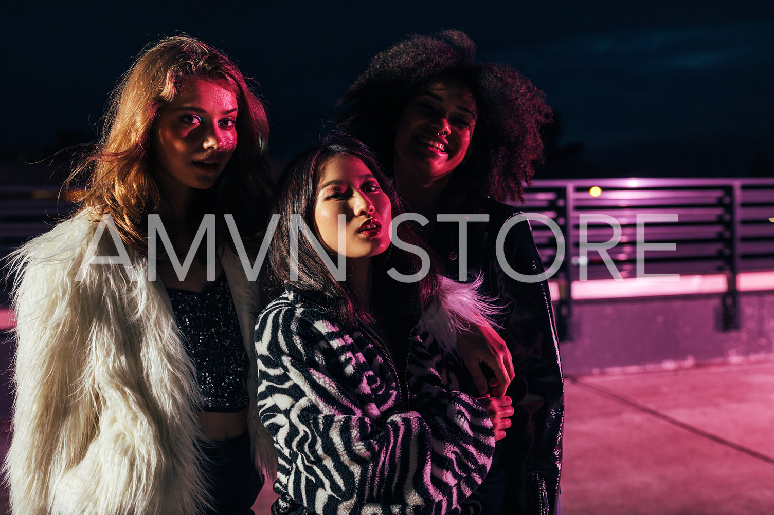 Thee stylish girls looking at camera under pink neon light	