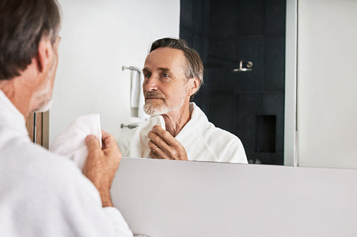 Mature man with beard holding a white towel doing morning skincare routine in the bathroom