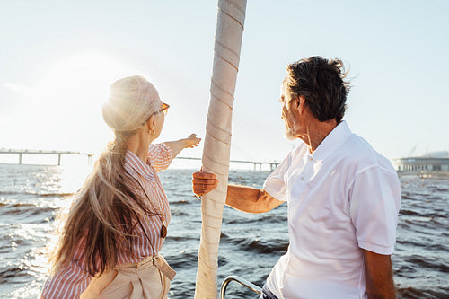 Rearview of two mature people sitting on a sailboat bow and enjoying summer day