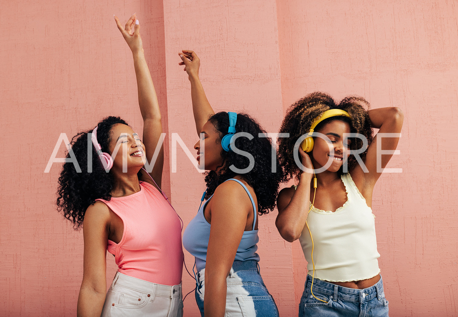 Three girlfriends with different body types dancing together. Smiling females with headphones enjoying music at pink wall.