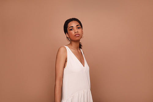 Young woman in a white dress against a brown background. Portrait of a female posing in the studio.