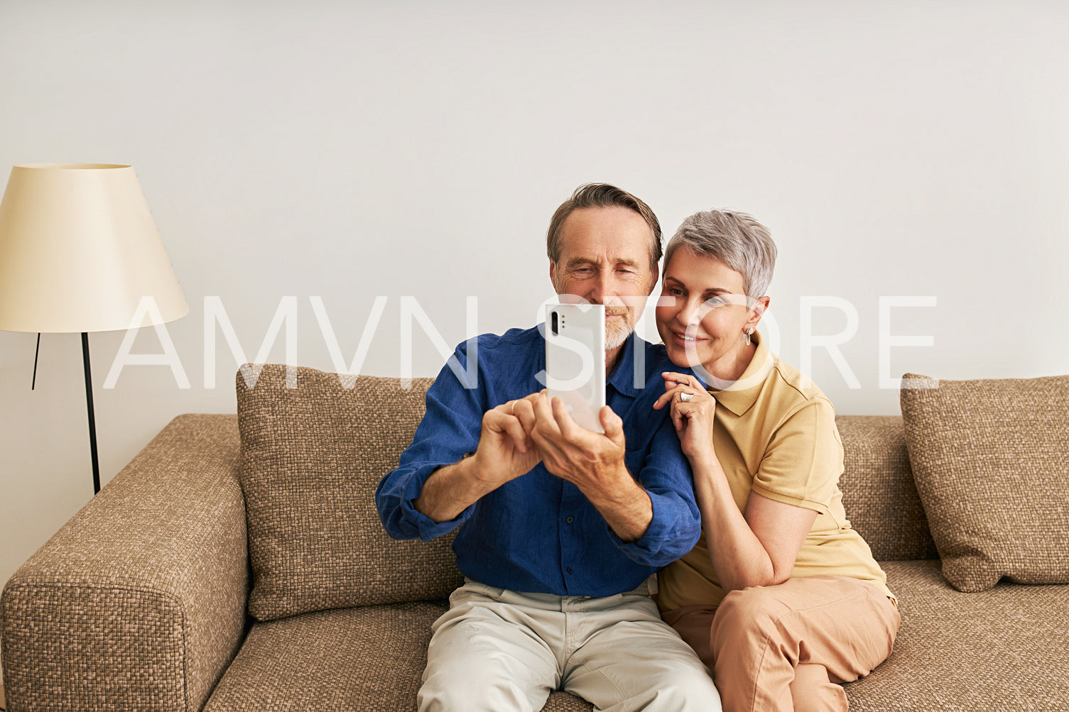 Senior couple in casuals at home sitting on couch taking a selfie	