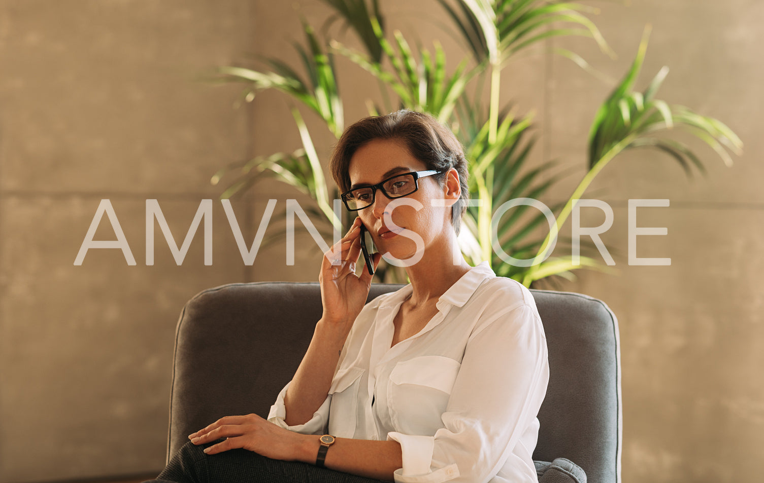 Middle-aged businesswoman in formal wear talking on mobile phone while sitting indoors