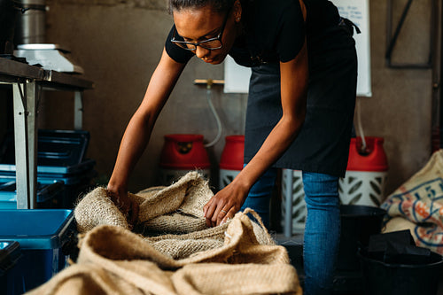 Female entrepreneur standing in storage, looking in a sack with fresh coffee beans