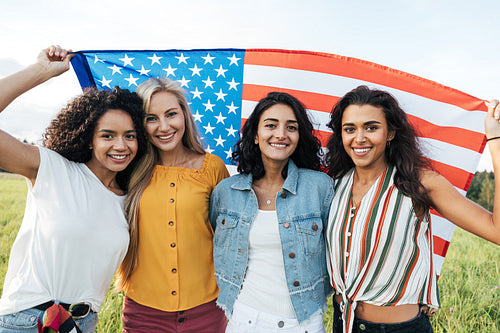 Group of multi-ethnic women holding a USA flag. Female friends celebrating independence day.