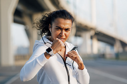 Young sportswoman training boxing moves outdoors. Woman practicing punches at evening on a city street.