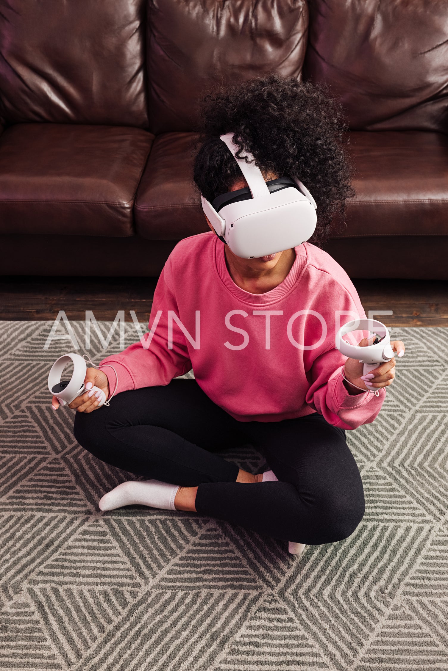 Young woman with curly hair sitting near a sofa and playing VR games