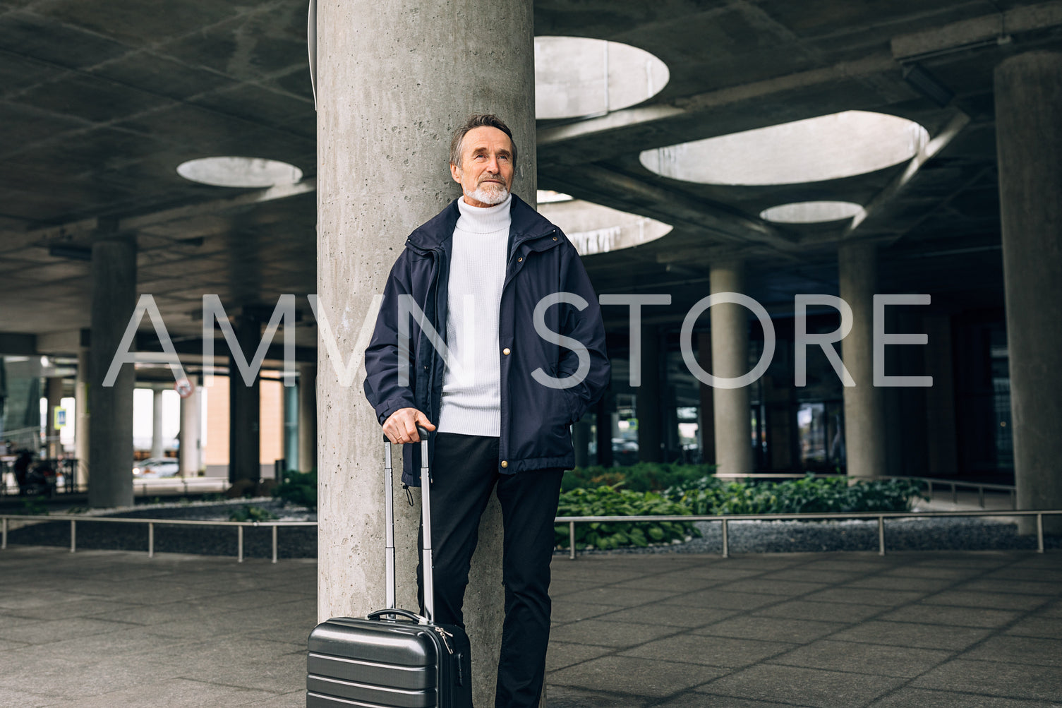 Businessman with rolling suitcase standing outdoors and looking away	