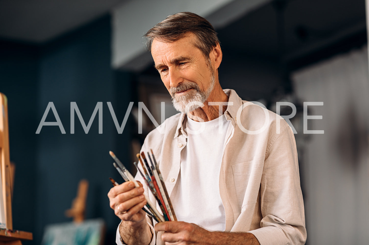 Portrait of senior painter holds a bunch of brushes choosing a one	