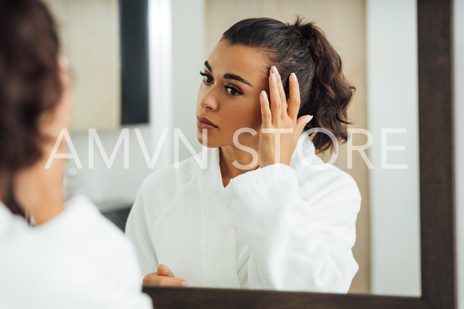 Beautiful brunette looking at reflection in the mirror and touching hair	