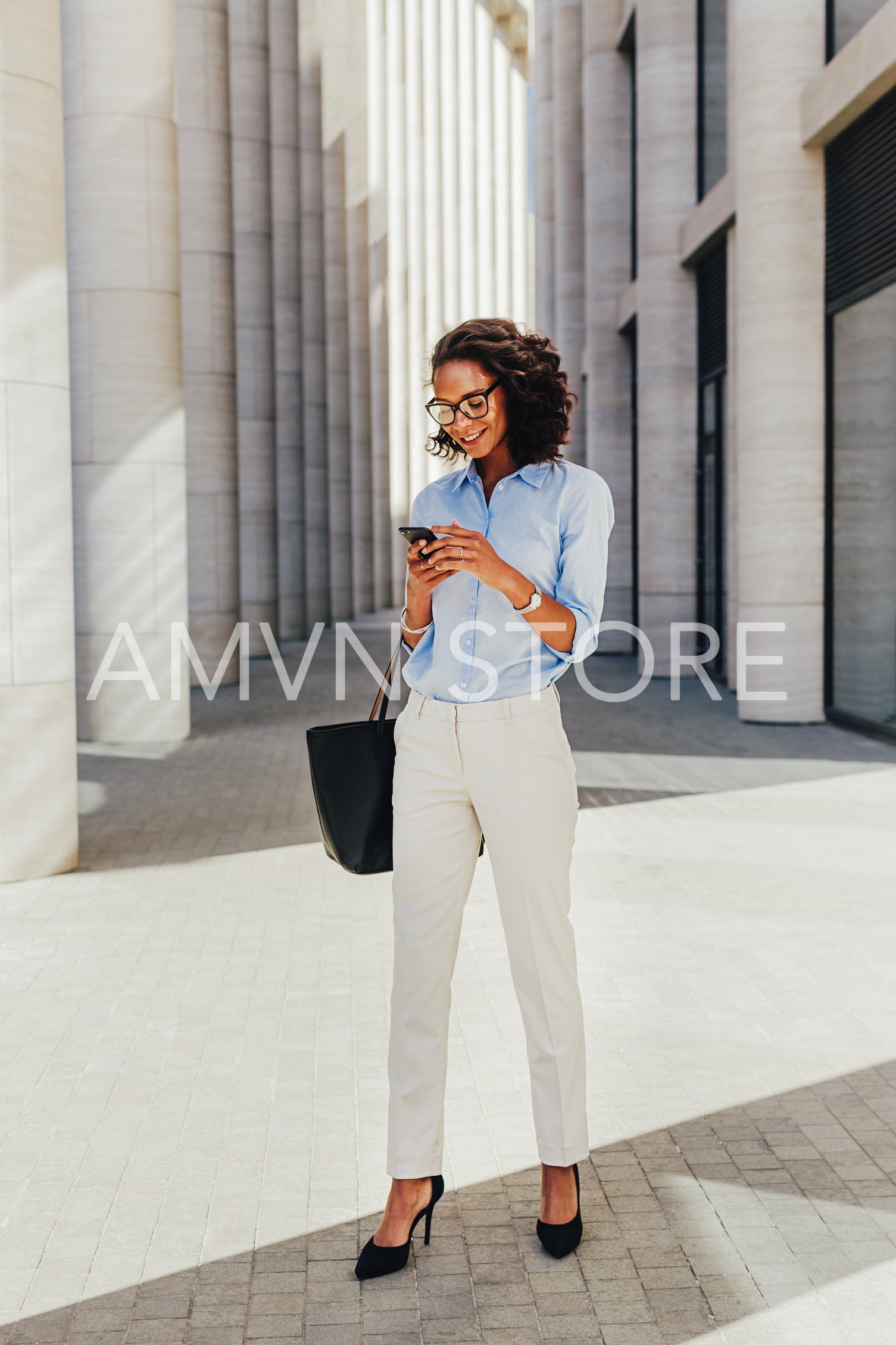 Businesswoman standing outside office building. Young professional using smartphone.