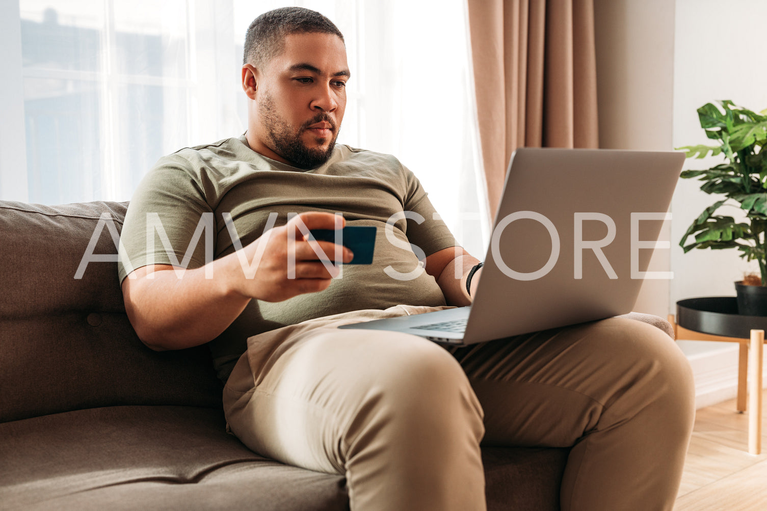 Young man paying online with a credit card at home. Mixed race male with a laptop on his hips making an internet order.	