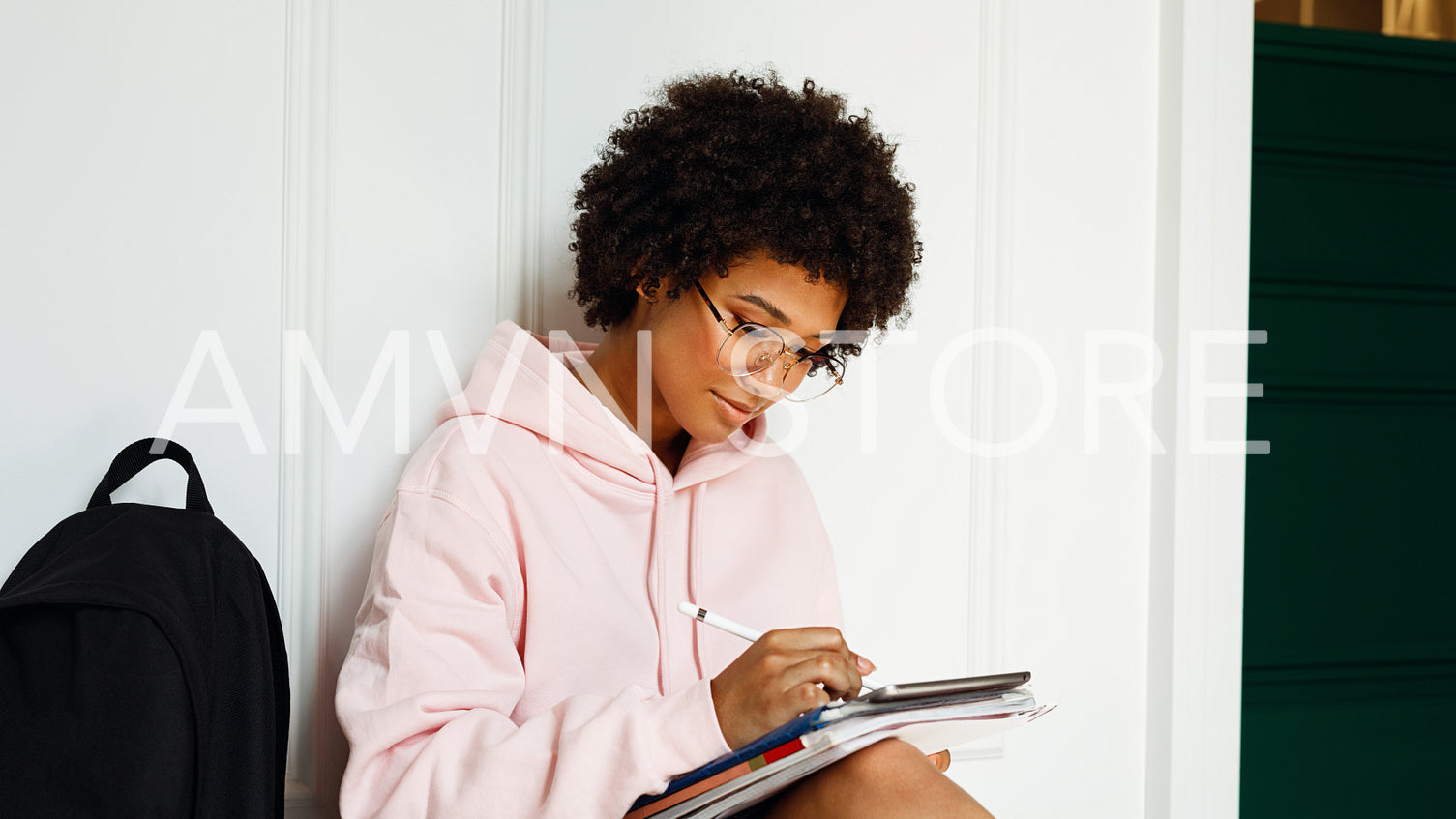 Side view of a girl sitting on floor and writing on digital tablet with stylus	