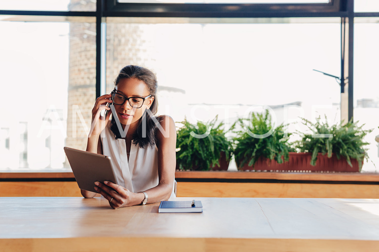 Young businesswoman looking on digital tablet while talking on smartphone	