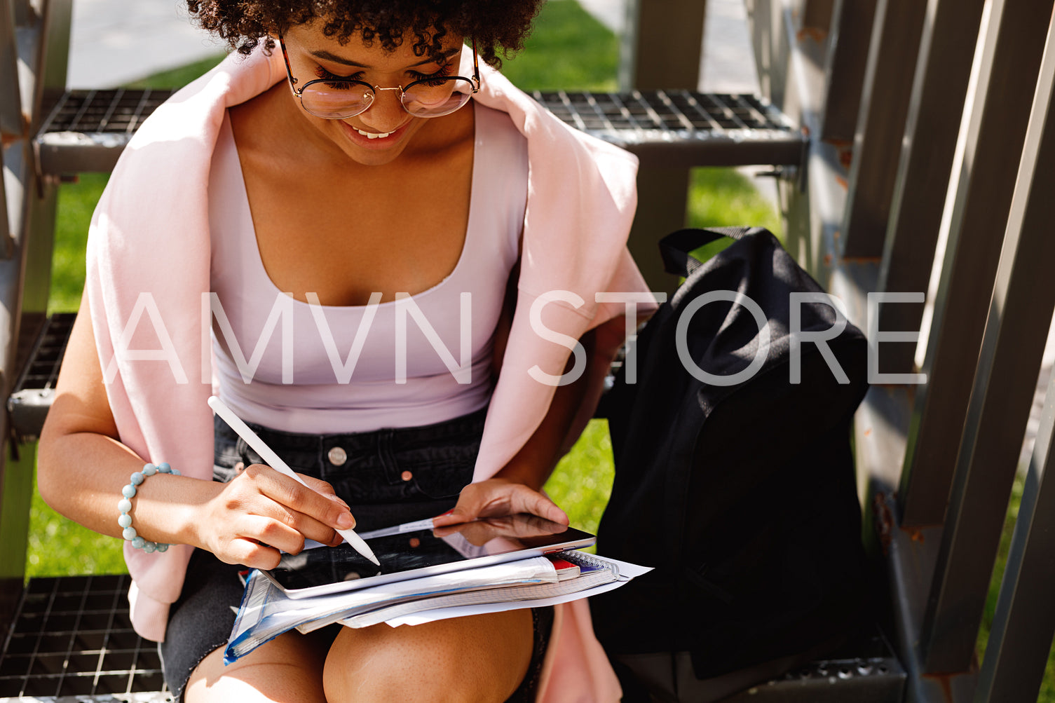 Young graphic designer sitting on stairs outdoors, working on digital tablet	