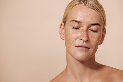 Portrait of a beautiful woman with perfect skin standing with closed eyes in studio against pastel background