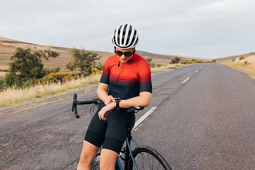 Woman cyclist in sportswear leaning on her bicycle checking smartwatch