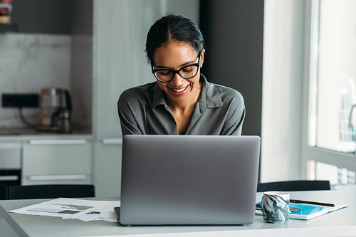 Smiling woman standing at the kitchen counter and working on a laptop computer from home