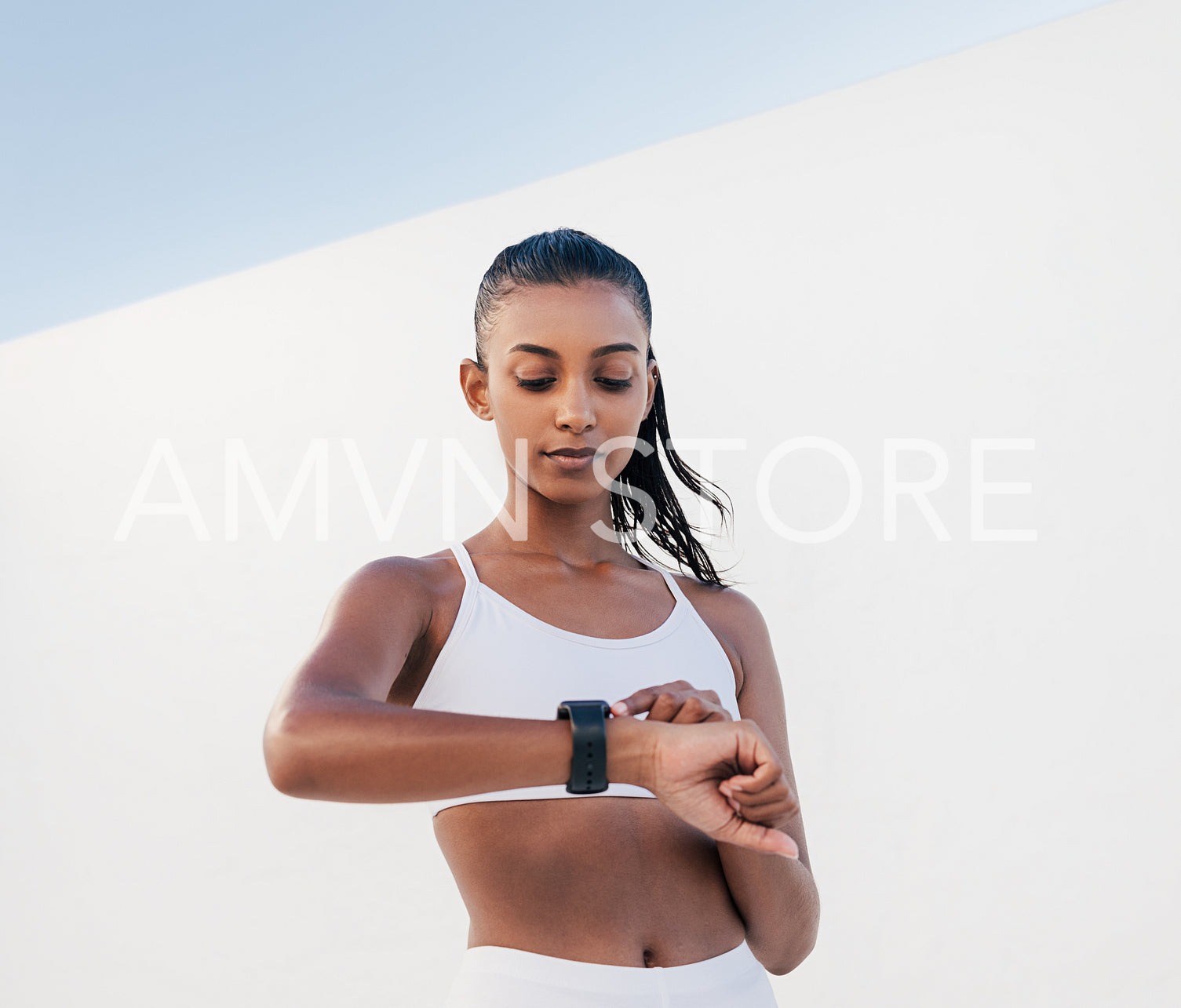 Portrait of a young female checking her pulse. Woman in a fitness bra adjusting her smartwatch.