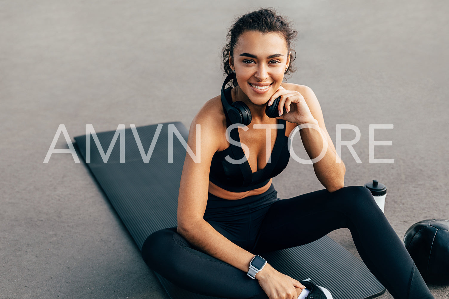 Portrait of a beautiful sportswoman with headphones sitting on a mat outdoors	