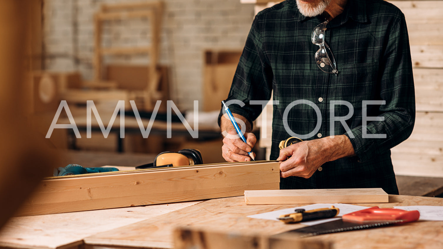 Mid section of male carpenter measuring and marking wood in workshop	