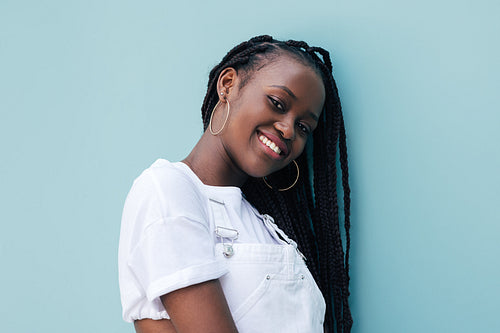 Portrait of young smiling woman with braids leaning on blue wall looking at camera