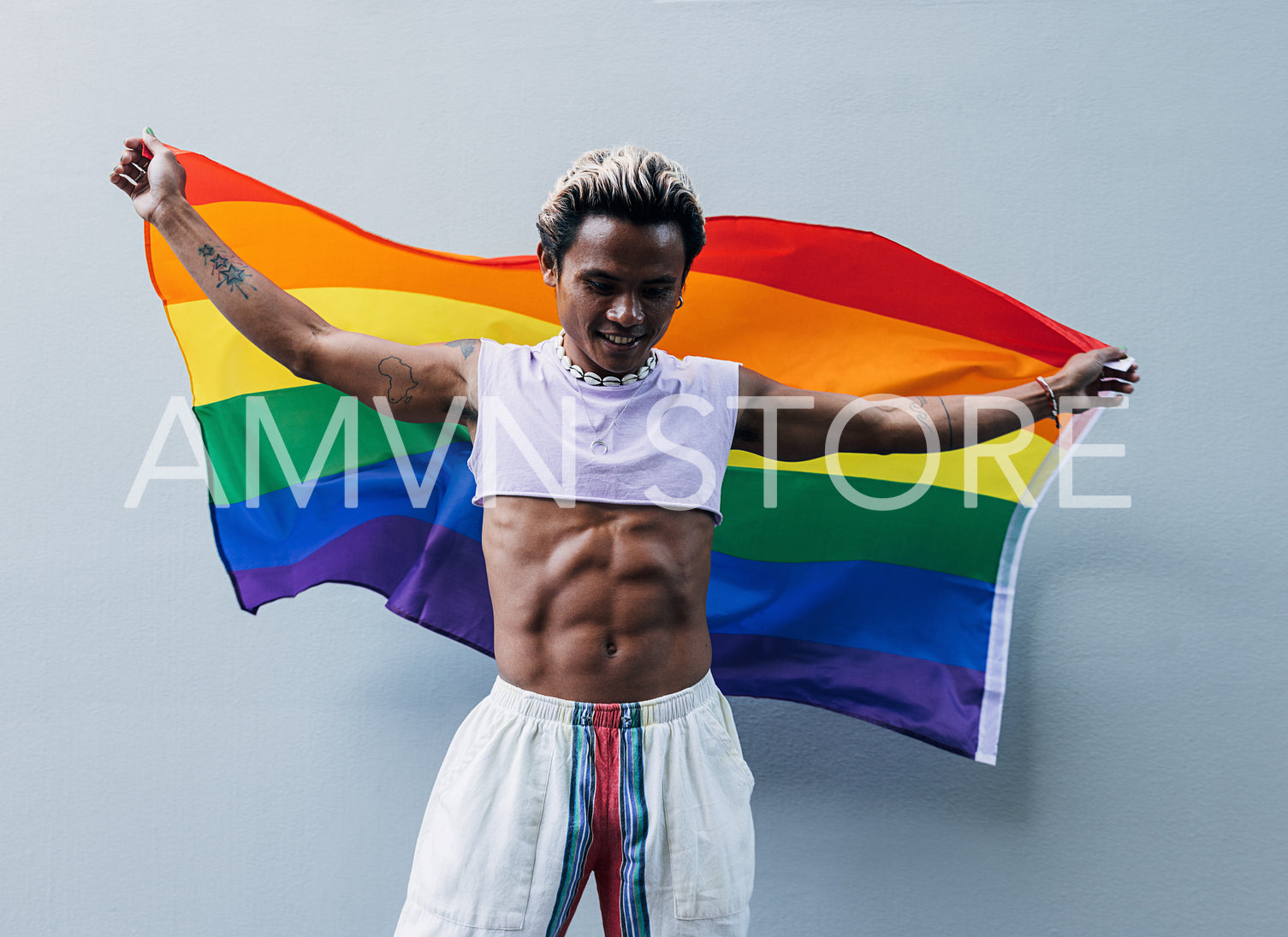 Happy muscular guy with LGBT rainbow flag at grey wall outdoors