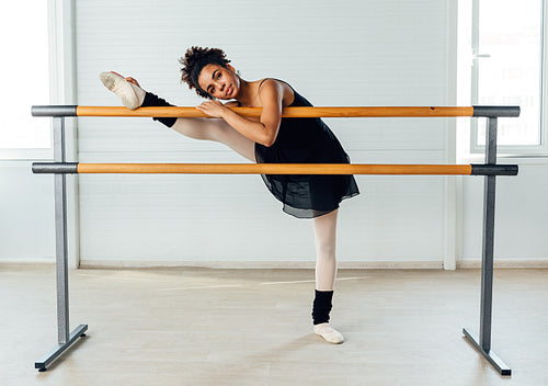 Young ballerina stretching her leg in dance studio. Woman doing exercise on ballet barre.