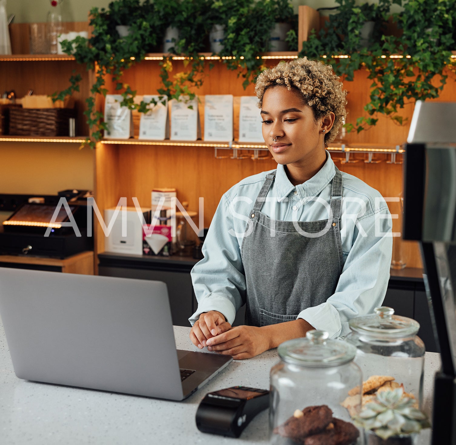 Young woman entrepreneur with laptop at the counter. Female in an apron working as a barista looking at a laptop.